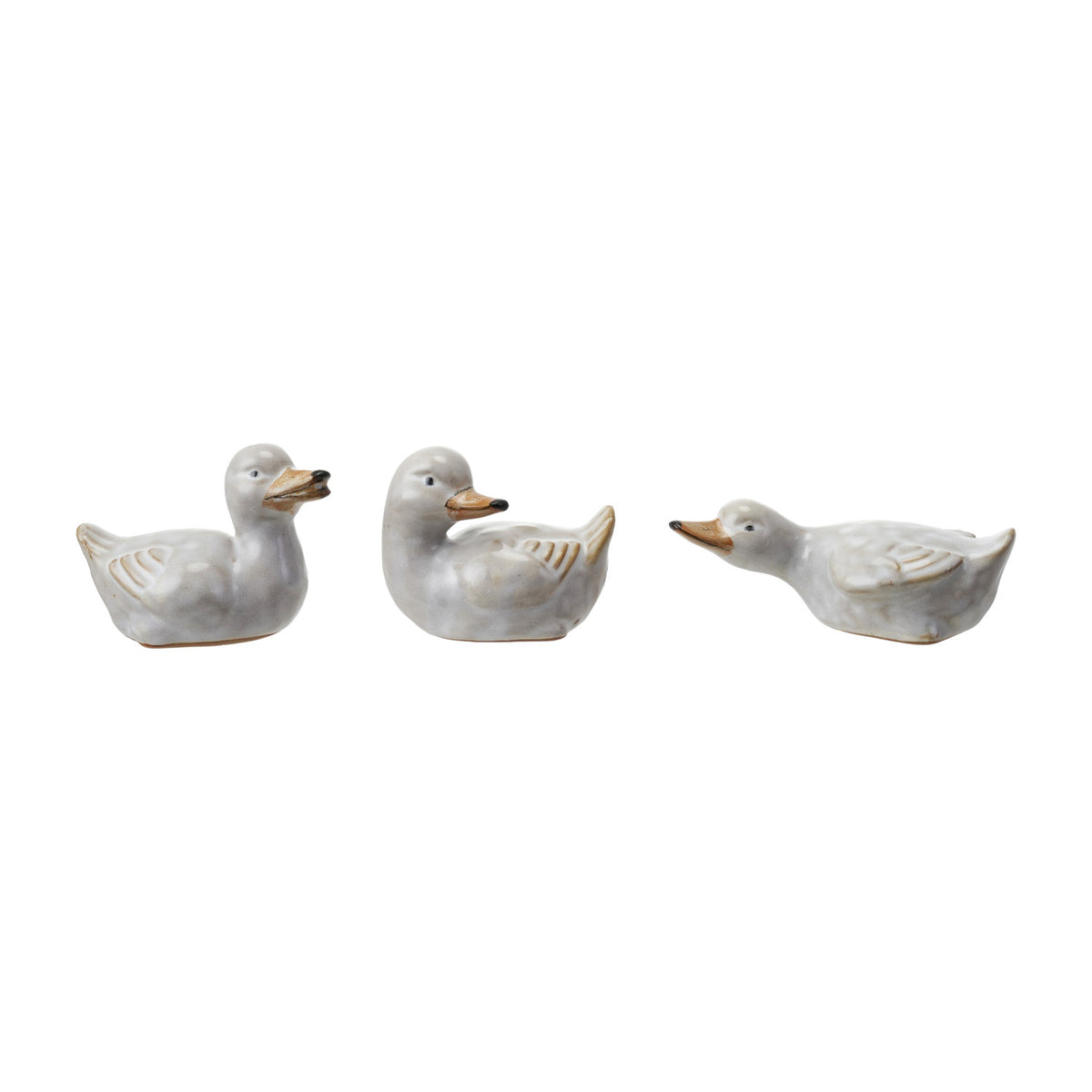 Three small ceramic duck figurines in different sitting poses, featuring a glossy white glaze with subtle gold and orange accents on the beaks and feather details, set against a plain white background.