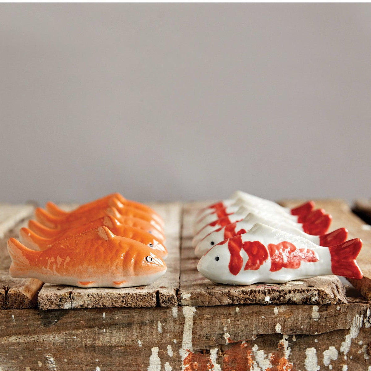 Two ceramic fish figurines, one orange and one white with red accents, on a wooden surface.