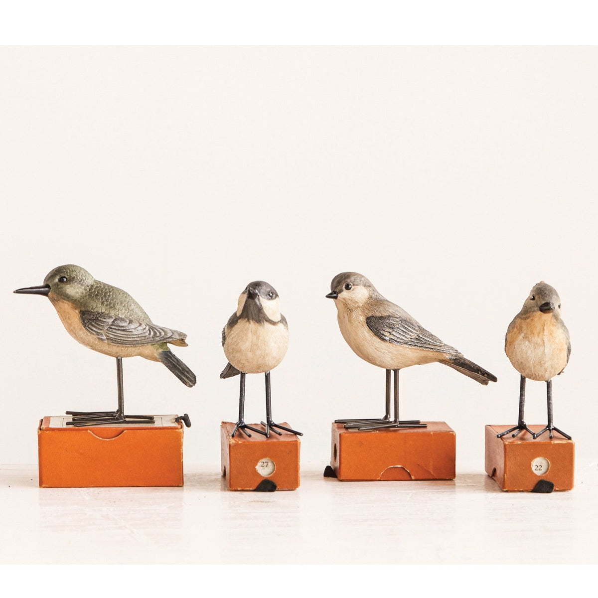 Four small bird figurines mounted on orange rectangular bases, arranged in a row against a plain off-white background.