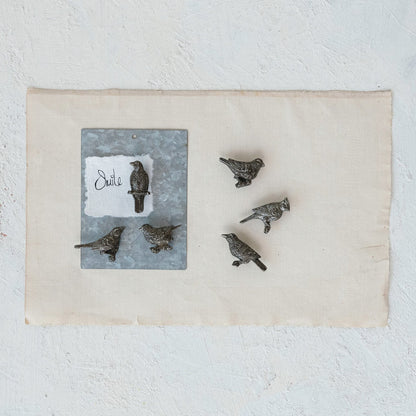 Set of bird-shaped magnets on a white surface with a decorative card featuring text.