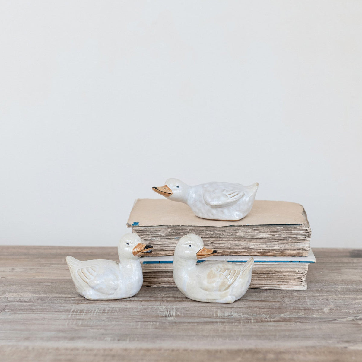 Three ceramic ducks on a stack of books with a light background
