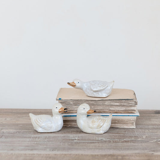 Three ceramic ducks on a stack of books with a light background